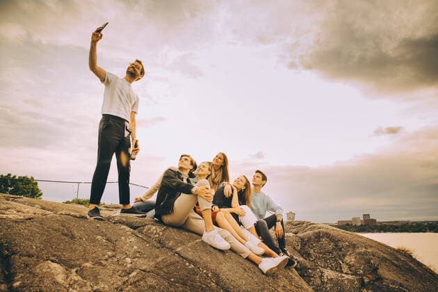 IMAGO Creative: Landleben - Alfresco, Draußen Man taking selfie with friends on rock formation against sky in picnic during sunset , model released Copyright: xMaskotx , MA75714