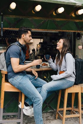 Full length of smiling friends holding coffee cups while sitting by concession stand in city , model released Copyright: xMaskotx , MA76007