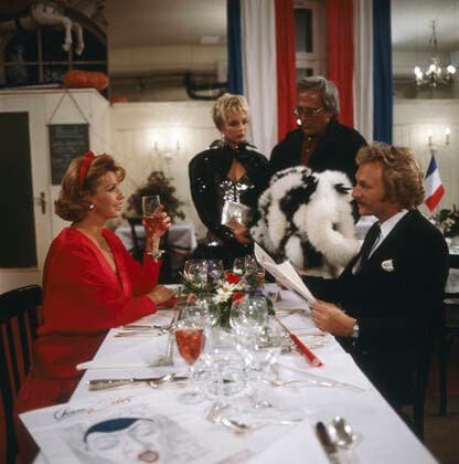 Kir Royal, 1986 Senta Berger als Mona und Franz Xaver Kroetz als Baby Schimmerlos sitzen im Restaurant, im Hintergrund, Corinna Drews als Lisa und Dieter Hildebrandt als Herbie in Kir Royal, Folge 1: Wer reinkommt, ist drin, Regie: Helmut Dietl, 1986. Senta Berger as Mona sitting at the table with Franz Xaver Kroetz as Baby Schimmerlos, in the background Corinna Drews as Lisa and Dieter Hildebrandt as Herbie in Kir Royal, Episode 1: Wer reinkommt, ist drin, Director: Helmut Dietl, 1986., Deutschland Copyright: kpa UnitedArchives55021038 EDITORIAL USE ONLY