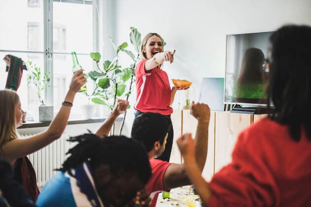 IMAGO Creative: FIFA WM 2022, Fußball Kultur Smiling woman pointing at friends while watching soccer match at home , model released, property released Copyright: xMaskotx , MA77393