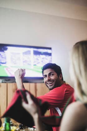 Smiling young man looking at female friend while watching soccer match at home , model released, property released Copyright: xMaskotx , MA77395