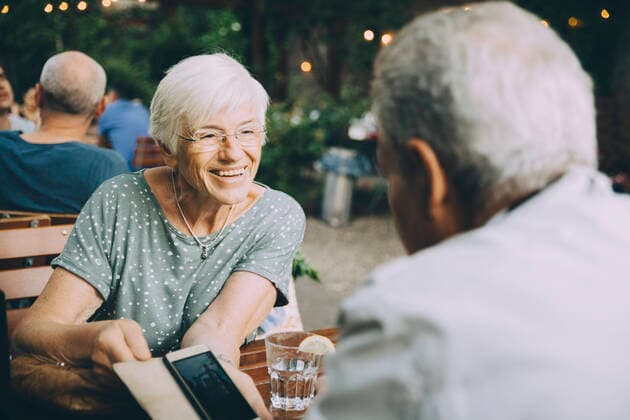 Smiling woman showing mobile phone to senior man while sitting at restaurant in city , model released Copyright: xMaskotx , MA78030