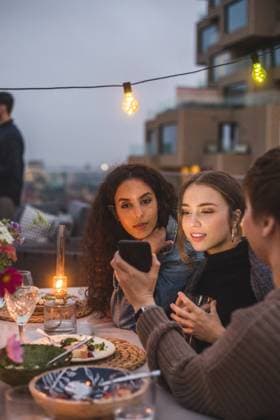 Woman showing smart phone to female friends during social gathering on building terrace , model released, property released Copyright: xMaskotx , MA78343