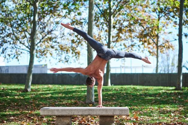 IMAGO Creative: Fit durch den Herbst Back view of unrecognizable shirtless guy in jeans doing handstand with legs spread wide on concrete gray bench in autumn park with fallen leaves Copyright: xJordixJanaux Model Released