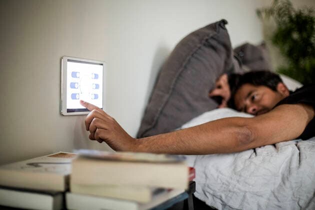 Man using digital tablet mounted on wall while lying on bed at smart home Sweden, Stockholm, model released, property released Copyright: xMaskotx , MA80376