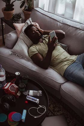 IMAGO Creative: Gesundheit, Burnout High angle view of man with headache using phone while lying on sofa at home Sweden, Stockholm, model released, property released Copyright: xMaskotx , MA80498