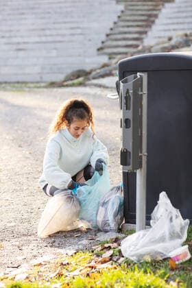 IMAGO Creative: Klimawandel - Umwelterziehung Female volunteer crouching with plastic waste by garbage can Sweden, Stockholm, model released Copyright: xMaskotx , MA81949