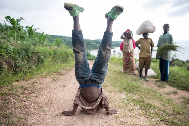Ruanda, Africa - December 14, 2019: African boy in casual wear break dancing standing on hands during work in plantation with other kids Copyright: xJuanxAlbertoxRuizx Model Released
