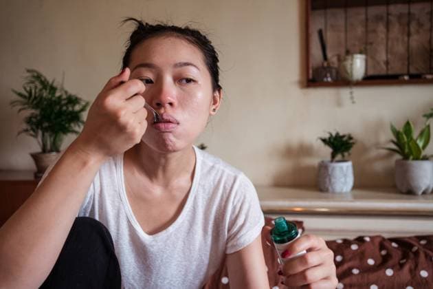 Sick Asian female sitting on bed in apartment and taking cough syrup while having flu Copyright: xJuanxAlbertoxRuizx Model Released