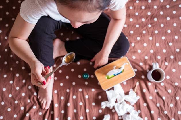 From above unrecognizable sick female sitting on bed in apartment and taking cough syrup while having flu Copyright: xJuanxAlbertoxRuizx Model Released