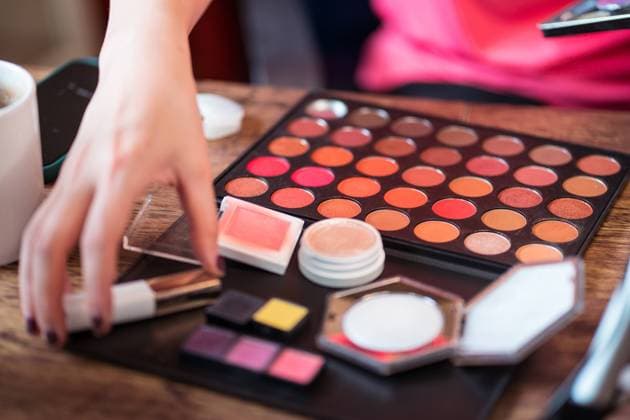 Crop anonymous female beauty blogger with colorful palette applying makeup while sitting at table in front of mirror and recording video tutorial Copyright: xJuanxAlbertoxRuizx Model Released