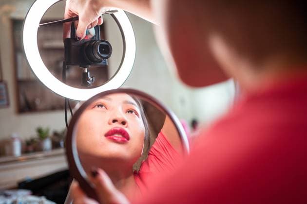 Young Asian female in casual outfit with manicure using camera and ring light while shooting video tutorial for beauty vlog in studio Copyright: xJuanxAlbertoxRuizx Model Released