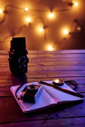 Black retro photo camera with notebook and film composed with vintage radio on wooden table in garland light, Model released Copyright: xJuanxGarciaxRisquezx MR