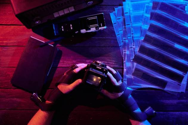 From above view of crop unrecognizable photographer with hands wrapped in film sitting at table with vintage photo cameras in dark studio, Model released Copyright: xJuanxGarciaxRisquezx MR