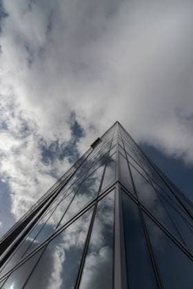 IMAGO Creative: Dichotomien, Reflexionen - Architektur Low angle of contemporary high rise building facade with glass exterior under white cloudy sky in modern city district Copyright: xJuanxLopezx Model Released