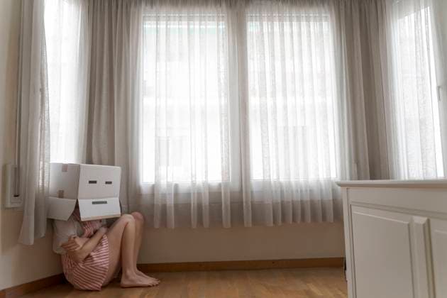 IMAGO Creative: Gesundheit, Magersucht, Bulimie Woman wearing a cardbox on head with bored smiley and cowering on the floor model released Symbolfoto property released AFVF06066