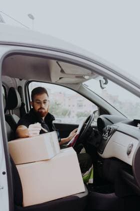 Attentive adult bearded courier in glasses preparing packages for transportation while sitting and marking boxes in car on blurred background during daytime, Model released Copyright: xLuisxMarioxHernandezx MR