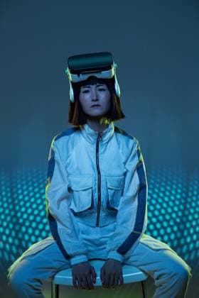Young woman with virtual reality goggles in forehead while sitting in a chair looking at camera with neon light Copyright: xManuelxRuizx Model Released