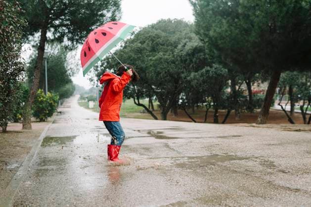 Side view active kid with watermelon styles open umbrella in red raincoat and rubber boots jumping playing in park alley in gray day, Model released Copyright: xMartaxMachinx MR