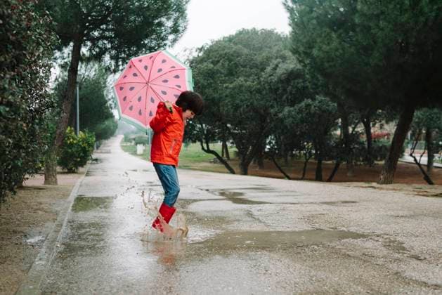 Side view active kid with watermelon styles open umbrella in red raincoat and rubber boots jumping playing in park alley in gray day, Model released Copyright: xMartaxMachinx MR