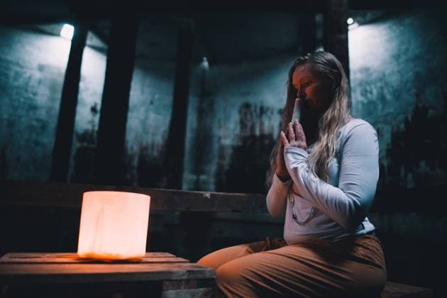Side view of young woman with praying hands sitting near lights in dark building, Model released Copyright: xMiquelxSuchx MR