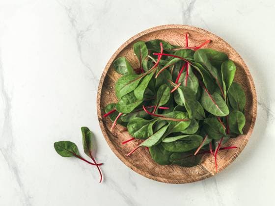 Fresh salad of green chard leaves or mangold on white marble background. Flat lay or top view fresh baby beet leaves on wooden plate. Copy space for text. Copyright: xOlgaxSergeevax Model Released