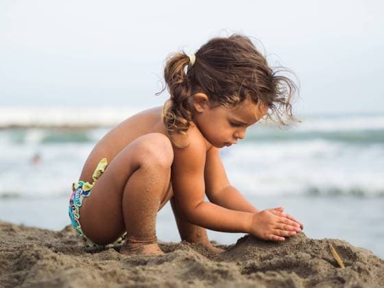 Side view of cute little girl with pigtails trying to make sand castle while playing on beach near waving sea on resort Copyright: xPatriciaxBecarotox Model Released