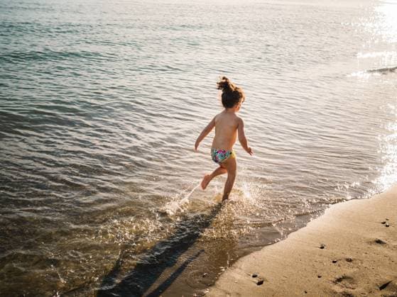 IMAGO Creative: 2021 Favoriten Back view of anonymous cute female kid in swimming slips running on sandy beach against calm sea Copyright: xPatriciaxBecarotox Model Released