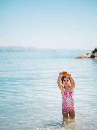 IMAGO Creative, Jahreszeit Sommer, Sommerferien Adorable toddler girl in swimming suit standing in warm water of calm sea playing with a seashell Copyright: xPatriciaxBecarotox Model Released