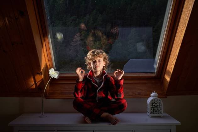 IMAGO Creative: Gesundheit, Stille Little boy in checkered pajama sitting near window in Lotus pose and meditating while looking at camera in morning at home Copyright: xPhilippexDegrootex Model Released
