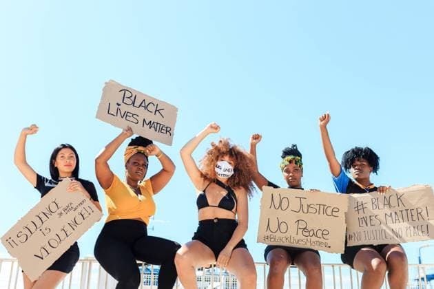Group of multiethnic female activists protesting with raised arms in city with carton placards with black lives matter inscription and looking at camera, Model released Copyright: xPicuaxEstudiox MR