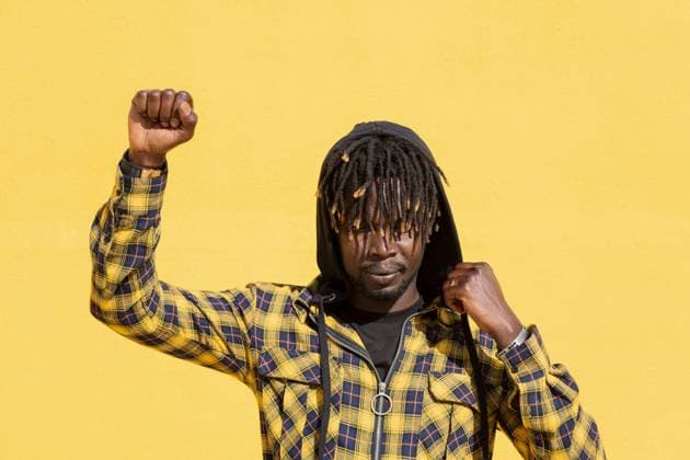 attractive young black man with raised fist and hood on an intense yellow background, concept of human rights struggle and lifestyle, copy space for text, Model released Copyright: xRaulxMelladox MR