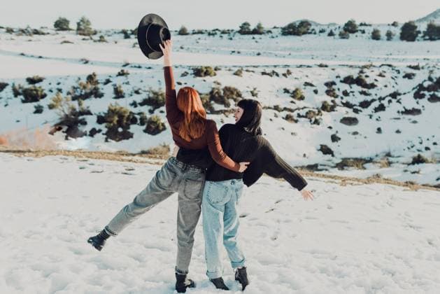 IMAGO Creative: Wintersport, Mode Back view of cheerful young female friends in casual clothes embracing and laughing while standing in snowy field in sunny day, Model released Copyright: xRemediosxPuertax MR