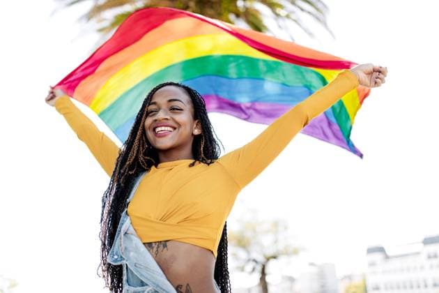 Low angle of proud African American female standing with fluttering LGBT rainbow flag on street and cheerfully looking away Copyright: xSergioxVictorxVegax Model Released