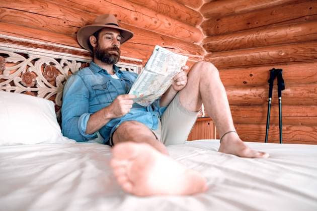 IMAGO Creative: Gesundheit, Stille Relaxed male tourist resting on bed in wooden house and finding route on paper map Copyright: xSergioxVictorxVegax Model Released