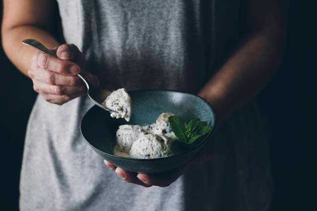 Crop view of anonymous woman with spoon in hand and holding bowl with stracciatella ice cream balls decorated with mint leaves Copyright: xVirginiaxMartinx Model Released