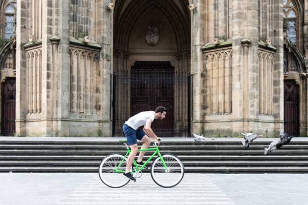 IMAGO Creative: Stadt-Dichotomien Side view of young man on green bicycle passing historic building in the city Copyright: xEgoitzxBengoetxeax Model Released