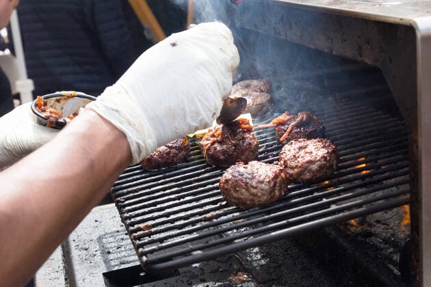 Beef burgers being grilled on food stall grill. Chef making beef burgers outdoor on open kitchen international food festival event. Street food ready to serve on a food stall.burger, grill, hamburger, street food, food, beef, stall, street, fast, meat, snack, outdoors, cuisine, seller, vendor, catering, lunch, meal, delicious, restaurant, junk food, sauce, outdoor, urban, event, making, chef, decorate, to go, take out, cart, plate, dressing, healthy, city, open kitchen, cheese, bacon, specialty, topping, pork, oven, stove, glove, fest, 