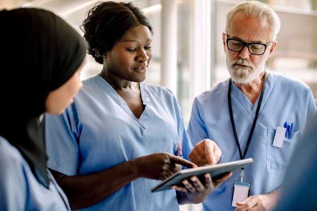 Smiling female nurse with digital tablet talking to colleagues in hospital Sweden, Stockholm, model released, property released Copyright: xMaskotx , MA83362