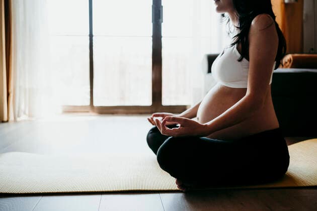 Pregnant woman meditating while sitting on exercise mat at home model released Symbolfoto property released EBBF01613