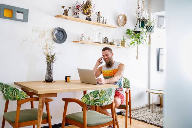 Mid adult man talking on smart phone while sitting by laptop in living room model released Symbolfoto property released IFRF00106
