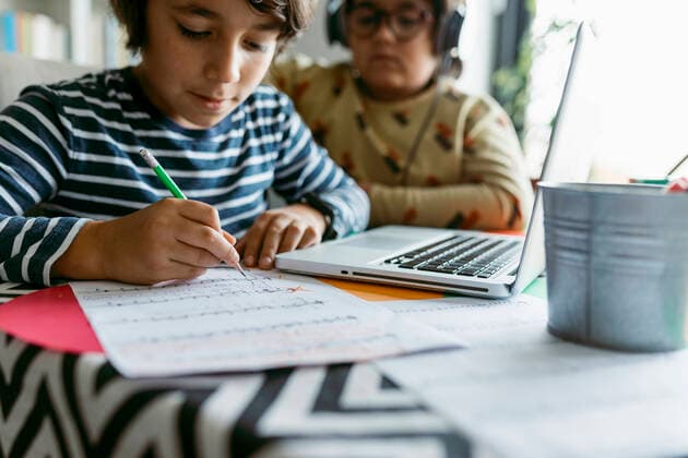 Boy completing homeschooling assignment while male friend sitting behind at table model released Symbolfoto property released VABF04026