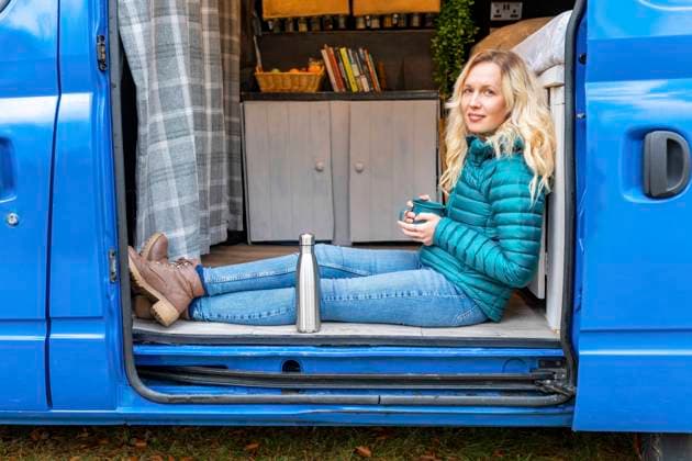 IMAGO Creative: Wintersport, Urlaub Smiling woman with tea cup relaxing at door of van model released Symbolfoto  WPEF03740