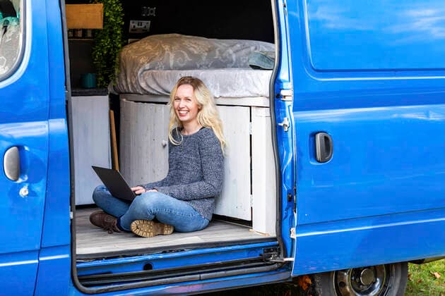 Happy woman with laptop sitting at door of camper van model released Symbolfoto  WPEF03779