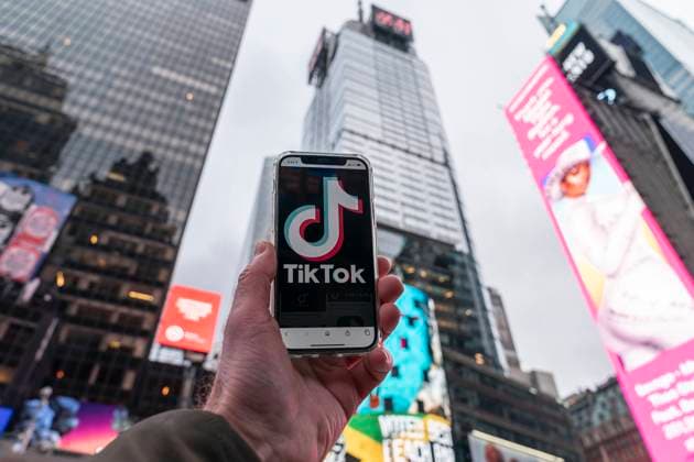 Business news from New York View of the building with person holding cell phone with TikTok logo where TikTok parent Bytedance reportedly agreed a 10-year lease of office space at 151 West 42st Street formely known as 4 Times Square. New York New York United States Copyright: LevxRadin