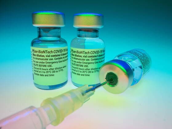 Cominarty BioNTech Pfizer Vaccine with mounted syringe in the vial and 2 additional vaccine vials with coloured background Variant 2 Copyright: xBEAUTIFULxSPORTS KJPetersx