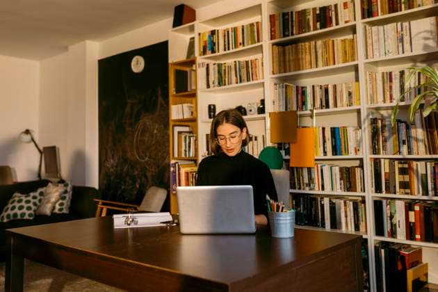 Female freelancer working on laptop sitting against bookshelf at home model released Symbolfoto property released VABF03817