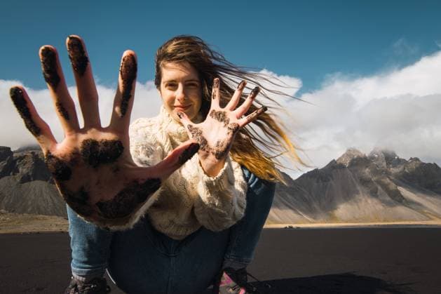 Beautiful woman with waving hair showing hands in black sand smiling at camera on background of mountains, Iceland., Model released Copyright: xKikexArnaizx MR