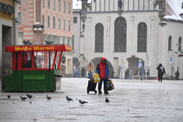 Theme picture Winter in the Coronavirus Pandemic Prolongation Lockdown until 31 January 2021 Empty streets and squares Only a few passers-by go over the Marienplatz in Munich on 12 01 2021 A homeless man walks with his belongings past a hot chestnut stand in the foreground cavorting pigeons people, passers-by