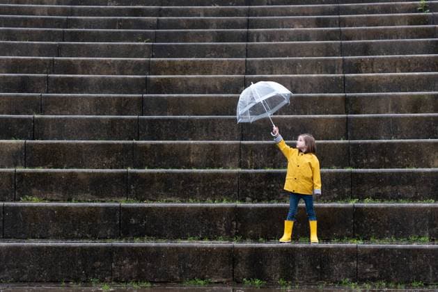 IMAGO Creative: Ende des Sommers Kid in yellow raincoat and rubber boots playing under umbrella along stone steps on rainy day in city Copyright: xEgoitzxBengoetxeax Model Released